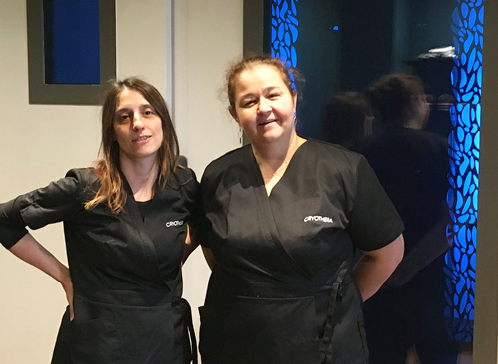 Portrait de Marie, psychothérapeute et associée du Centre Cryothérapies Le Mans, et de Séverine, infirmière. Les 2 femmes vêtues de leur blouse noire posent devant la chambre de cryothérapie corps entier