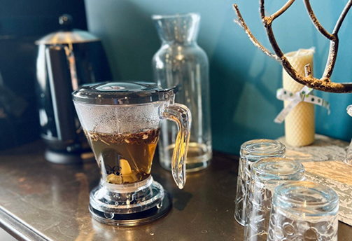 Gros plan sur une infusion aux plantes dans une tasse transparente posée sur une étagère dans le salon détente du centre Cryothérapies Le Mans.